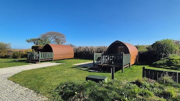 Deux cabanes en bois, de style « capsule », dotées d’espaces de détente extérieurs, entourées d’une pelouse bien entretenue et d’un chemin de gravier.