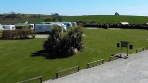 Een grasveld met een grindpad dat naar een poort leidt, omringd door geparkeerde campers.