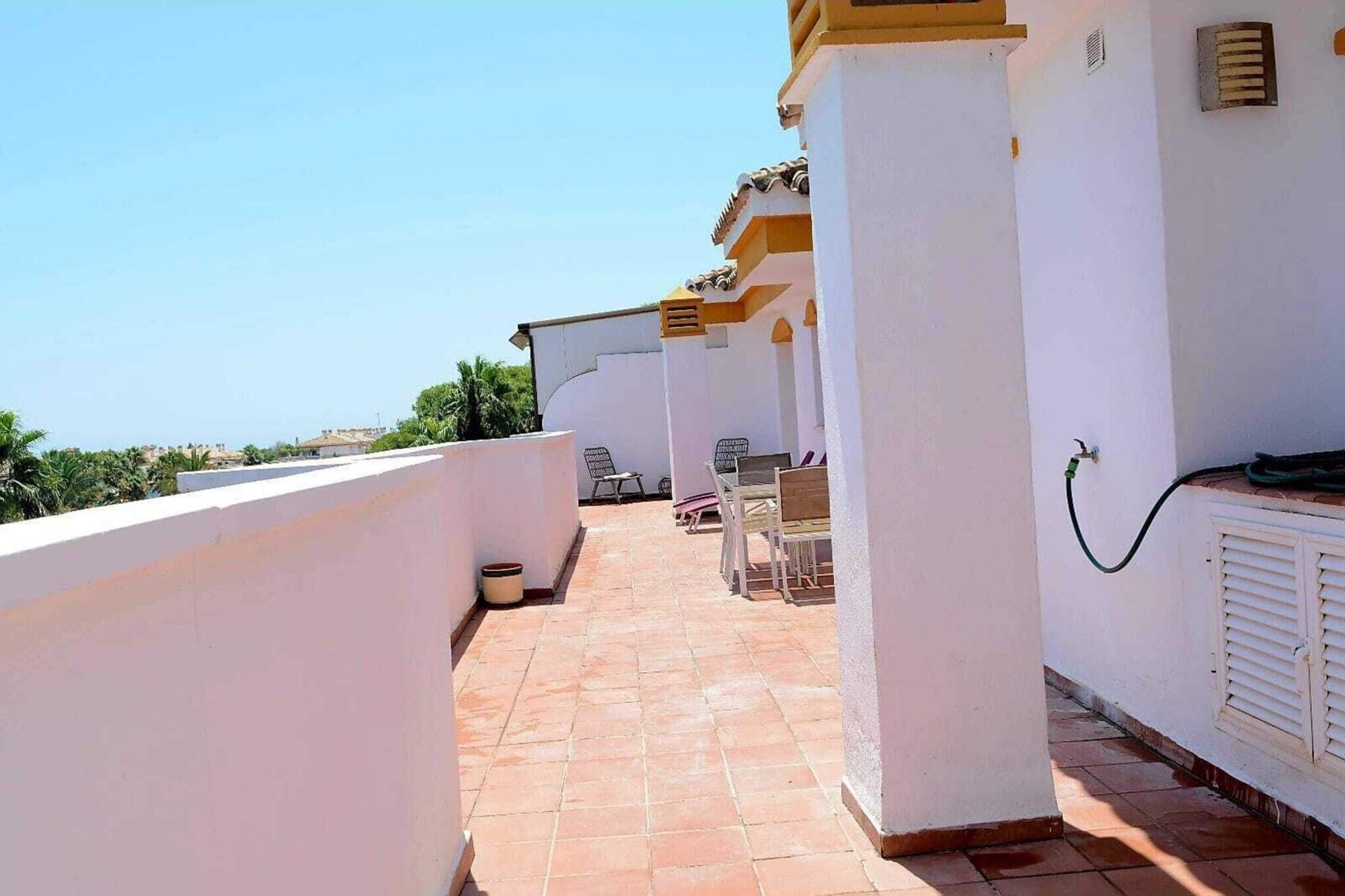 A covered outdoor area with a tiled floor, white walls, and a view of the sea.