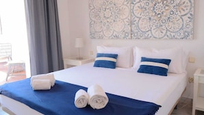 Una cama con ropa de cama blanca y azul, un plaid azul y dos toallas enrolladas.