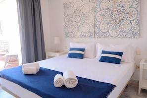 Ein Bett mit weißer und blauer Bettwäsche, einer blauen Tagesdecke und zwei aufgerollten Handtüchern.