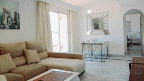 Una sala de estar con un sofá, una mesa de comedor con sillas, un espejo grande y un cuadro en la pared.