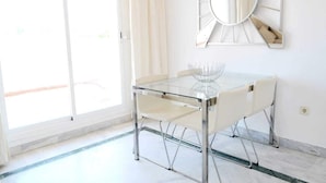 Un comedor moderno con una mesa de vidrio, sillas blancas, un espejo decorativo y vistas a través de un ventanal.