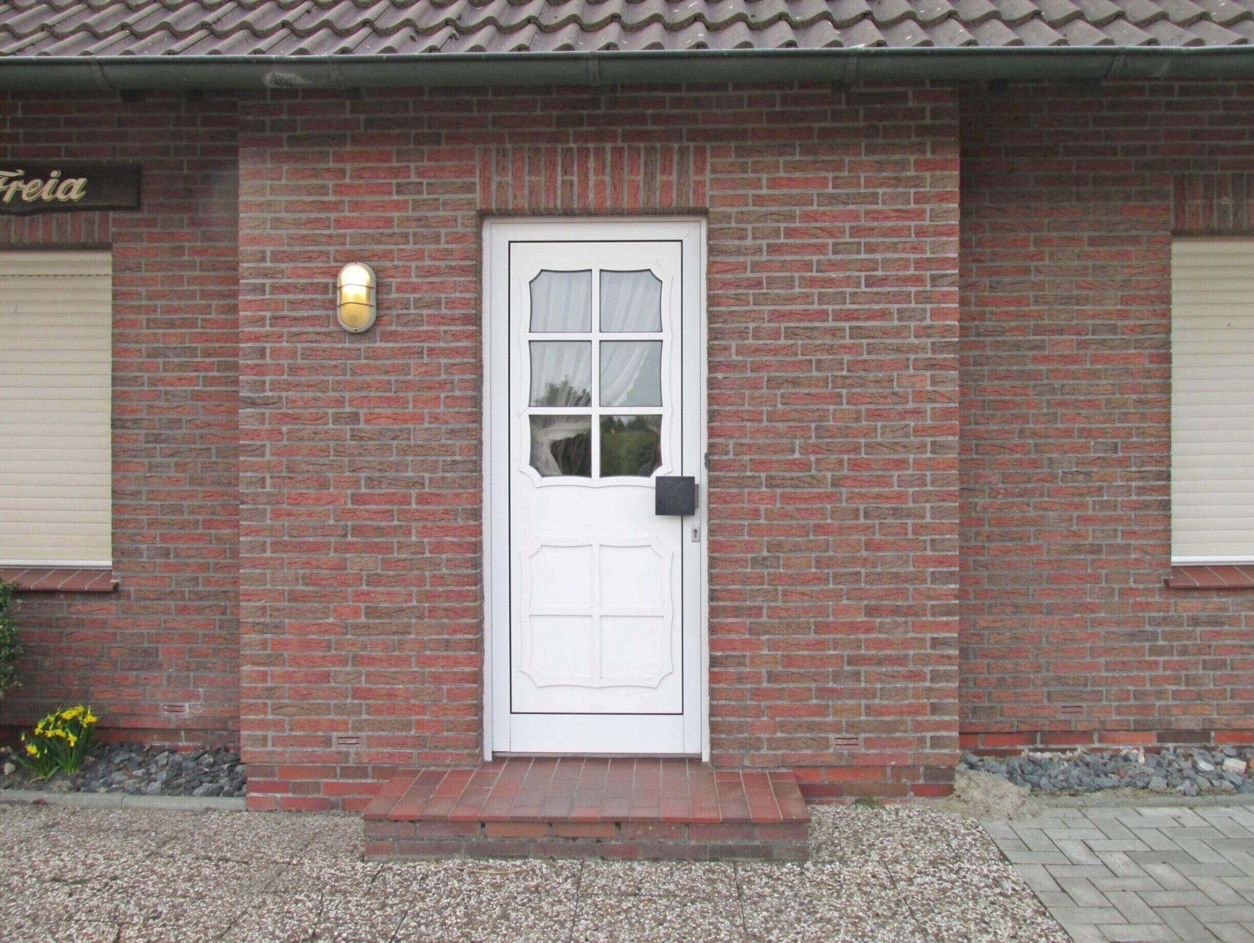 A brick building with a white door, a small porch, and a sign above the door.