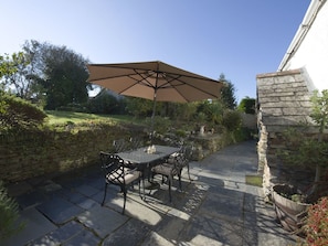 Eine Terrassengruppe mit Tisch und Stühlen unter einem großen Sonnenschirm, umgeben von Steinmauern und Pflanzen.