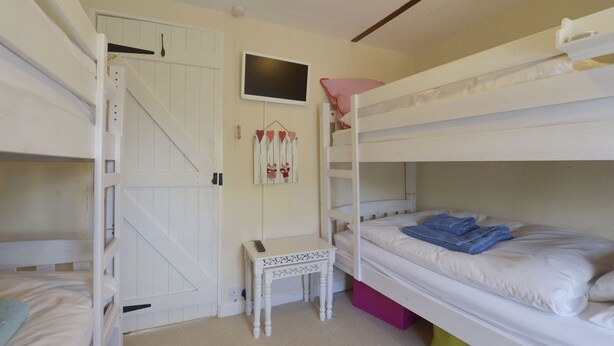 A bunk bed room with a door, a small table, and a wall decoration. - Mays Cottage (Wadebridge)
