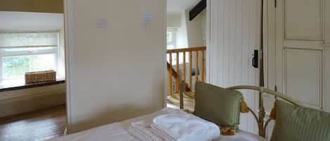 A bedroom with a bed, a window with a basket, a door, and a staircase.