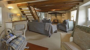 A cozy living room with a fireplace, wooden beams, and comfortable seating. - Mays Cottage (Wadebridge)