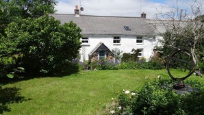 A white house with a grey roof, surrounded by a well-maintained garden with various plants and flowers. - Mays Cottage (Wadebridge)