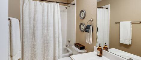 A bathroom with a shower curtain, toilet, sink, and a mirror.
