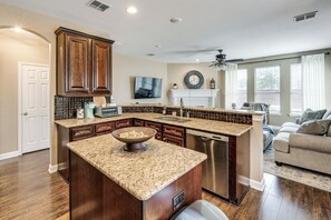 A kitchen with granite countertops, wooden cabinets, a dishwasher, and a large island with a bowl.