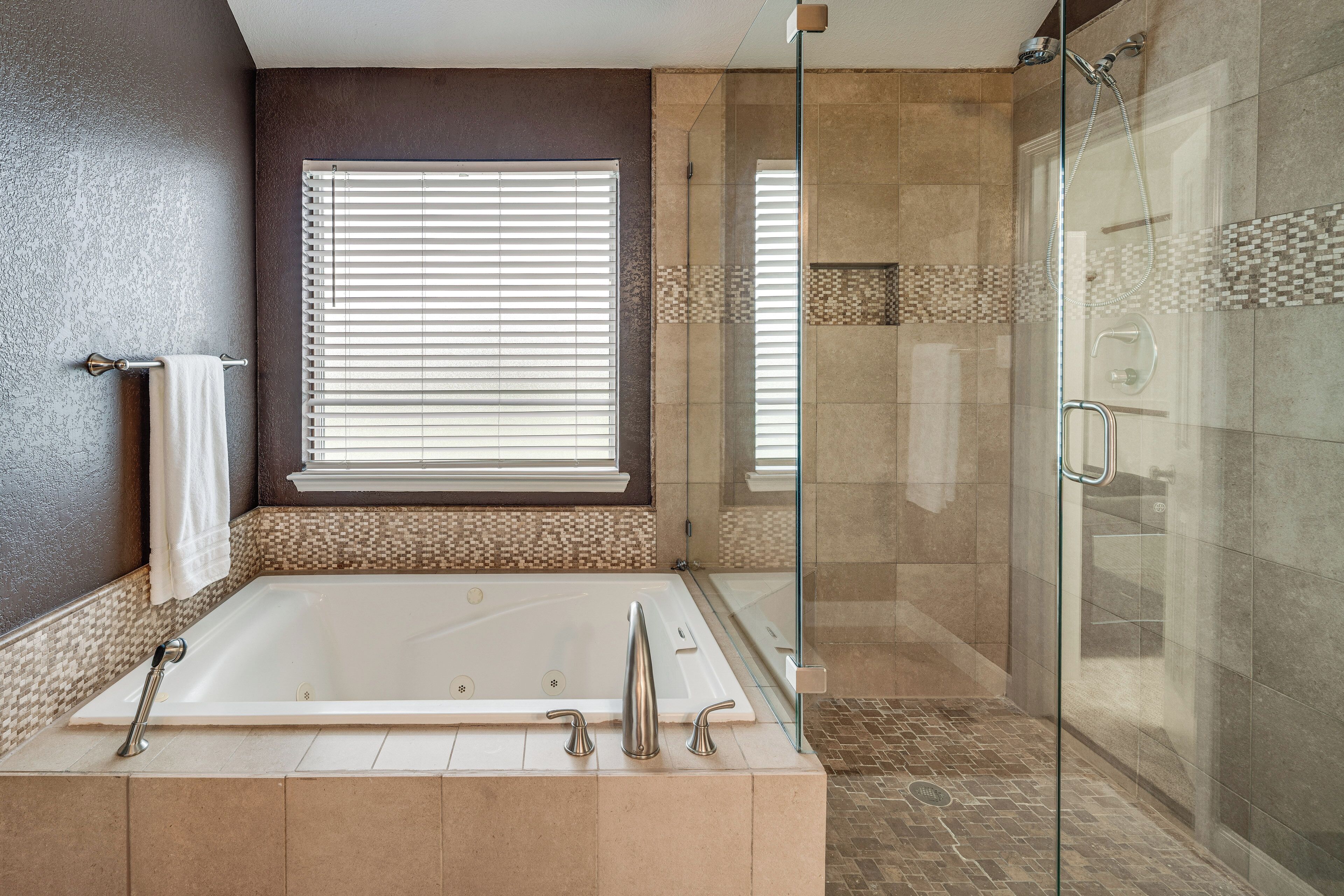 Un baño moderno con ducha envuelta en cristal, una bañera grande y una ventana con persianas.