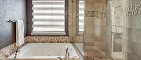 Un baño moderno con ducha envuelta en cristal, una bañera grande y una ventana con persianas.