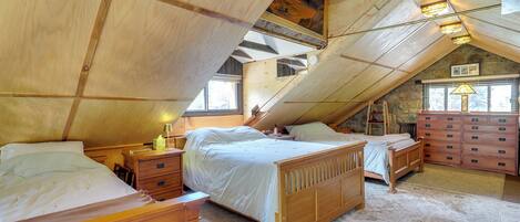 A bedroom with a sloped ceiling, wooden furniture, a dresser, and a window.