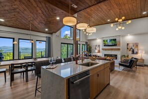 A spacious kitchen with a large island, wooden ceiling, and large windows offering a view of the outdoors. - Summit Splendor | Steps to The Trillium, Indoor Pool, Playground, Views! (Sevierville)
