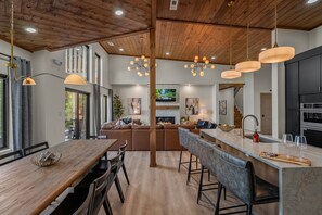 A modern kitchen with a central island, a dining area with a wooden table, and a living space with a fireplace. - Summit Splendor | Steps to The Trillium, Indoor Pool, Playground, Views! (Sevierville)