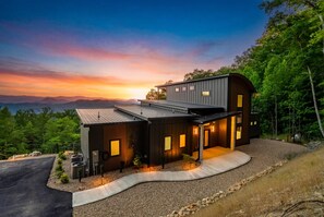 A modern two-story house with a curved driveway, a covered outdoor area, and a view of the mountains. - Summit Splendor | Steps to The Trillium, Indoor Pool, Playground, Views! (Sevierville)