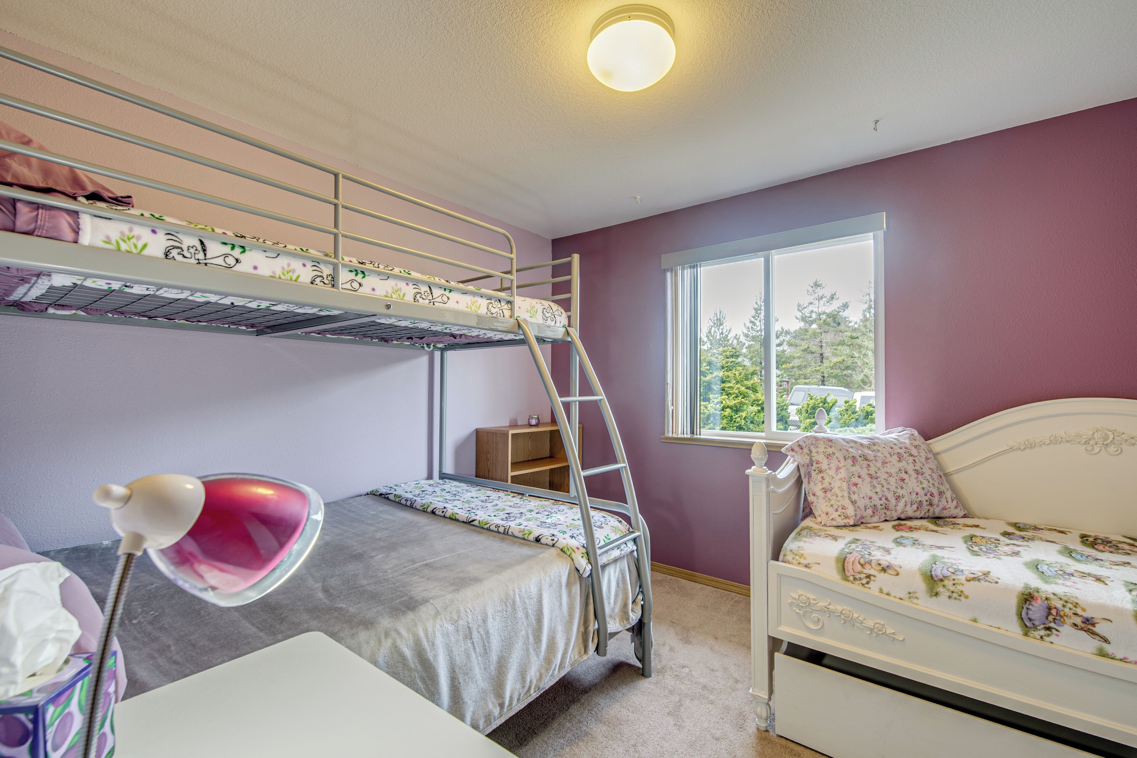 A bunk bed room with a window, a desk with a lamp, and a white bed.