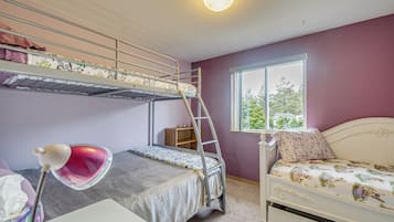 A bunk bed room with a window, a desk with a lamp, and a white bed.