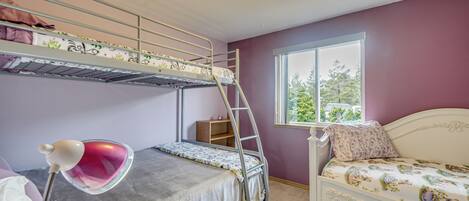 A bunk bed room with a window, a desk with a lamp, and a white bed.