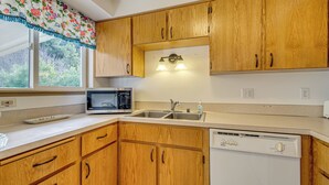 A kitchen with wooden cabinets, a microwave, a dishwasher, and a window with a floral curtain. - Ocean City Home w/ Fenced Yard: 1 Mi to Beach! (Ocean Shores)