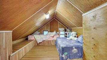 An attic bedroom with a sloped ceiling, wooden walls, a bunk bed, a desk, and a chair.