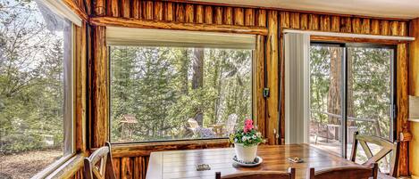 A wooden interior with a dining table and chairs, large windows, and a view of the forest.
