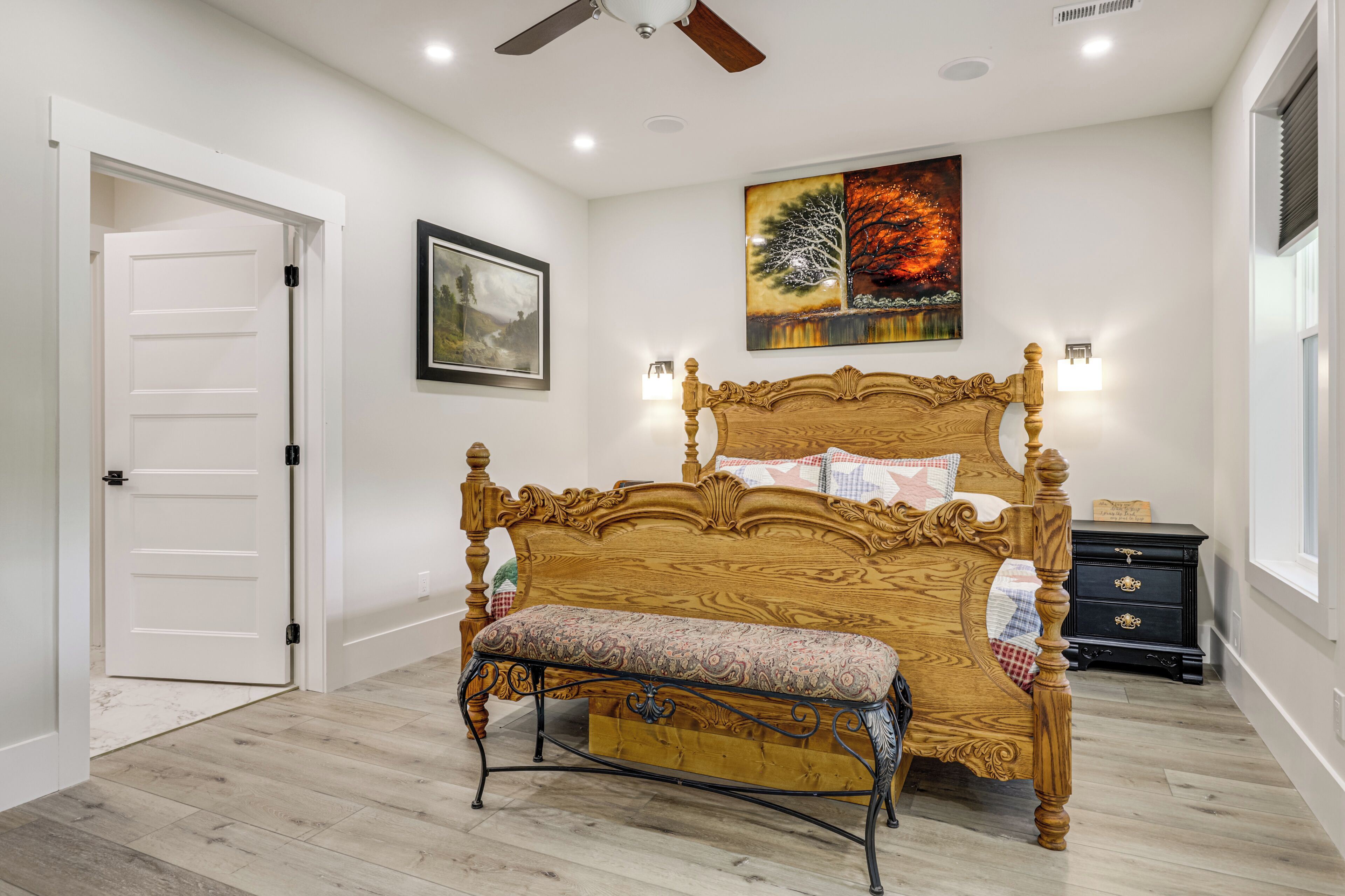 A bedroom with a wooden bed, a bench, a nightstand, a wall-mounted lamp, and a ceiling fan.