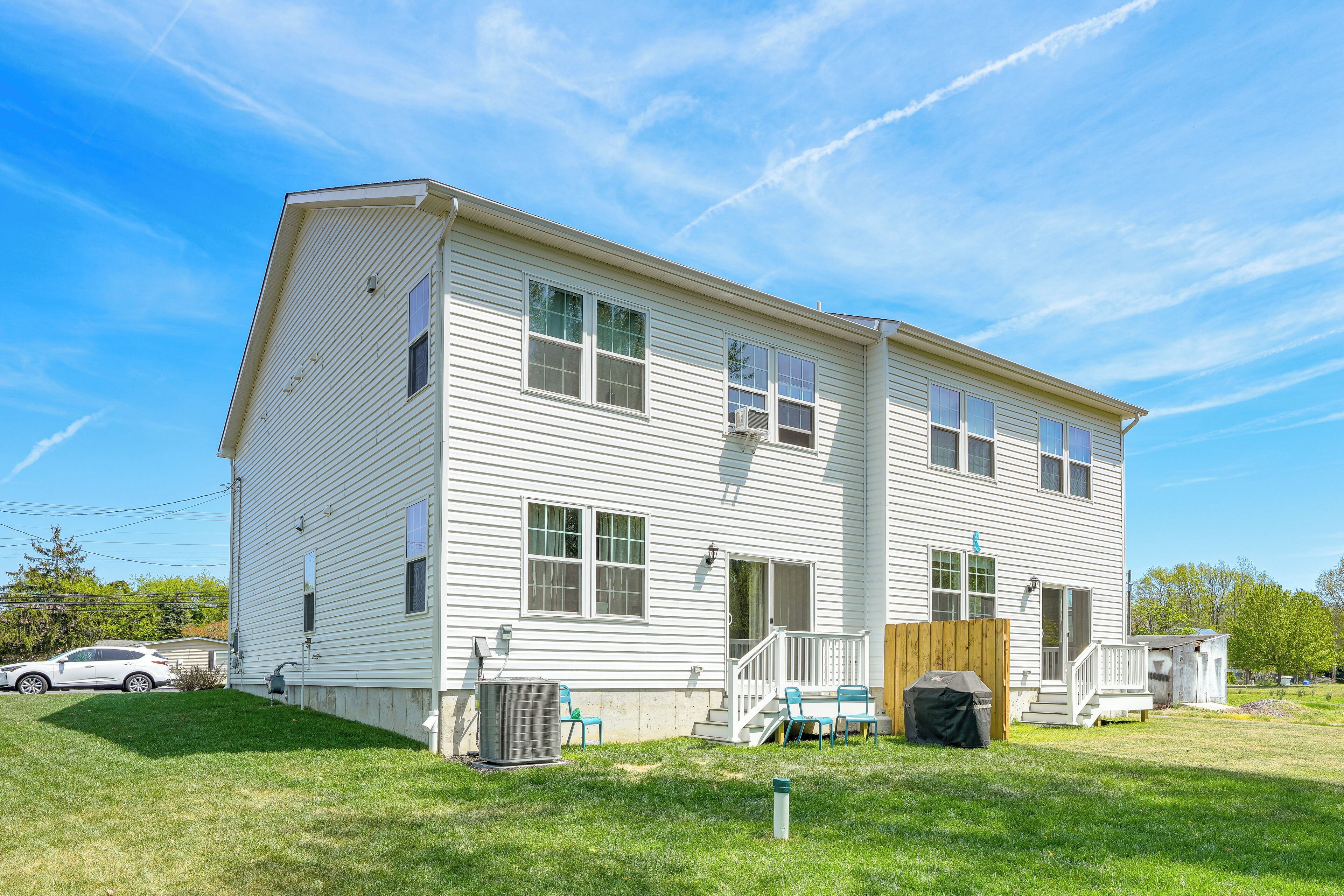 A two-story house with a front porch, a small deck, and a backyard with a lawn and a grill.