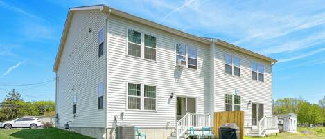 A two-story house with a front porch, a small deck, and a backyard with a lawn and a grill.