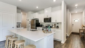 A modern kitchen with white cabinetry, a central island with stools, stainless steel appliances, and a wooden floor. - Family-friendly Cape May Retreat Near the Beach (Cape May)