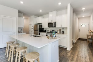 A modern kitchen with white cabinetry, a central island with stools, stainless steel appliances, and a wooden floor.