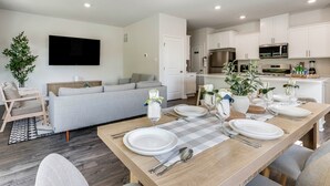 A modern living room with a dining area set for a meal, a flat-screen TV, and a kitchen with white cabinets and appliances. - Family-friendly Cape May Retreat Near the Beach (Cape May)
