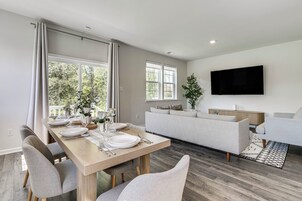 A modern living room with a sofa, a dining table set for four, and a flat-screen TV mounted on the wall.