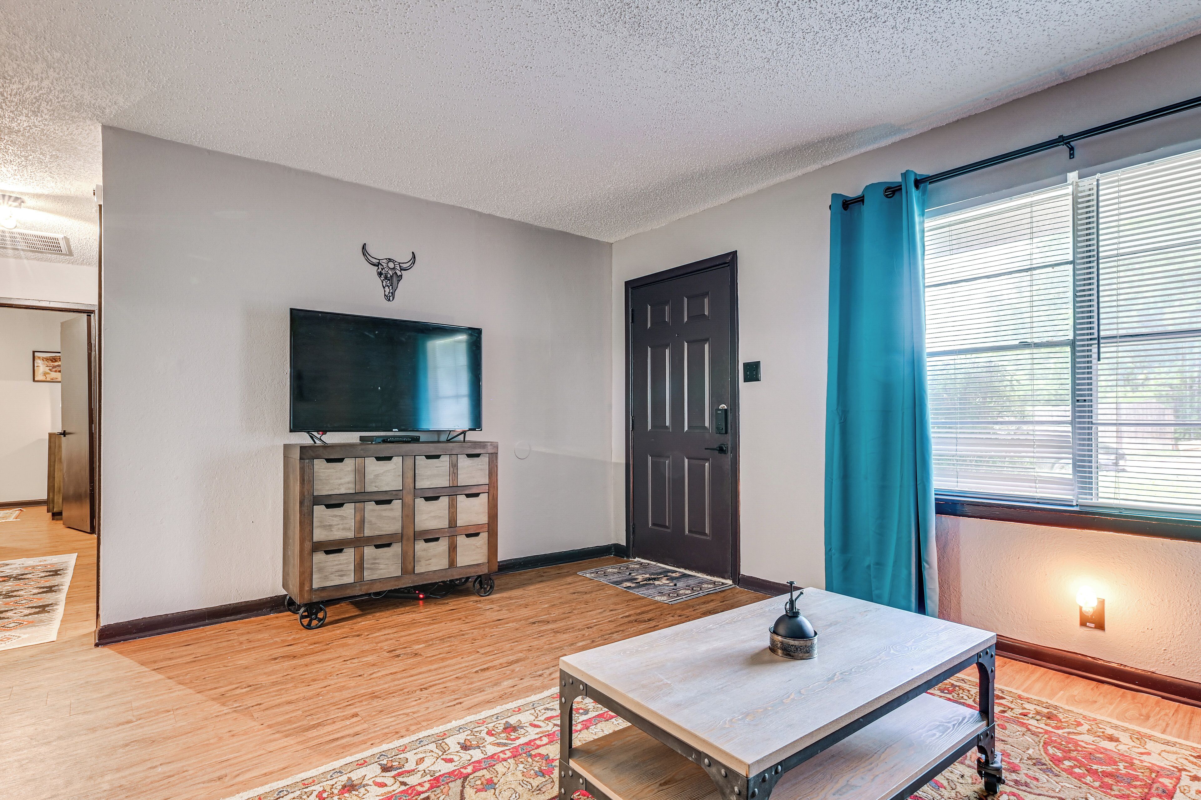 A room with a television on a wooden cart, a door, a window with curtains, and a patterned rug.
