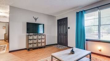 A room with a television on a wooden cart, a door, a window with curtains, and a patterned rug.
