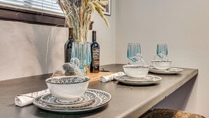 Een eettafel met een vaas droogbloemen, een fles en drinkglazen.