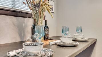 A dining table with a vase of dried plants, a bottle, and glassware.