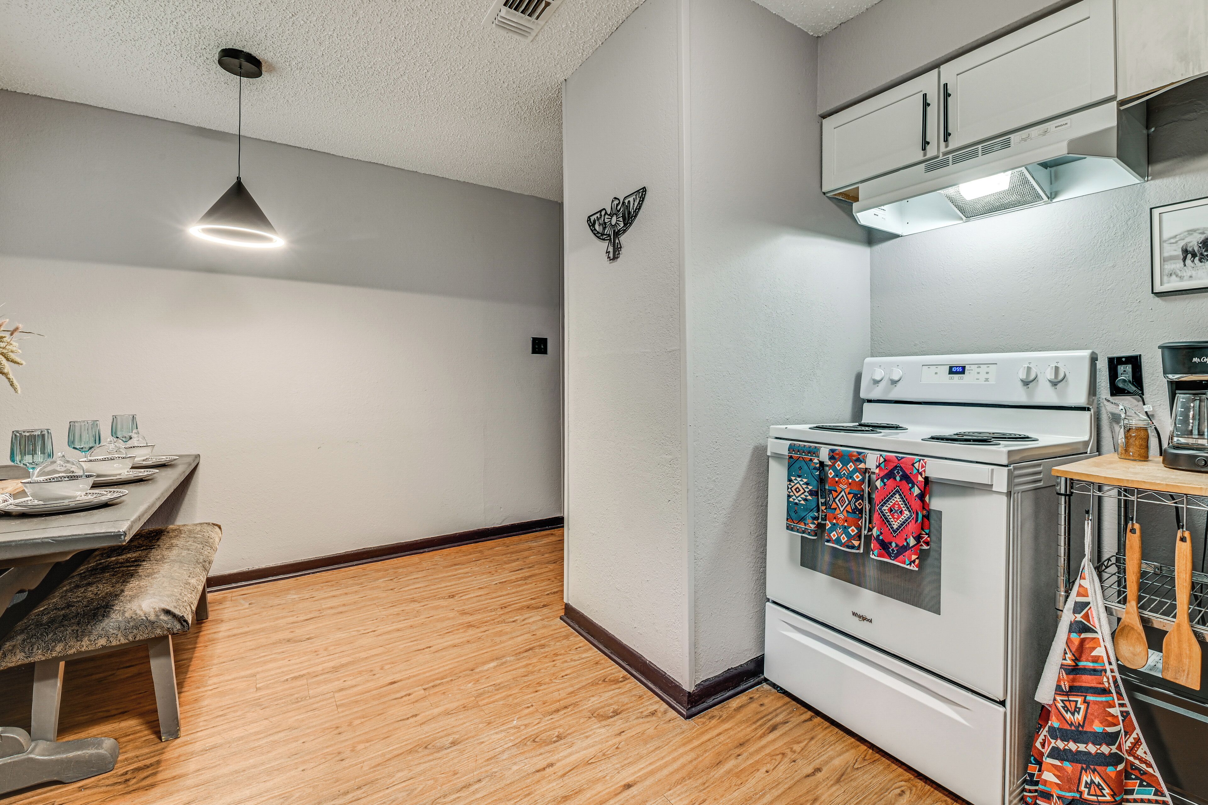 A kitchen with a white stove, wooden floor, and a hanging light fixture.
