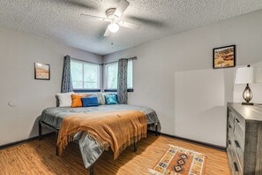 Ein Schlafzimmer mit einem Bett, einem Deckenventilator, einem Fenster mit Vorhängen, einem Schminktisch und einem Teppich.
