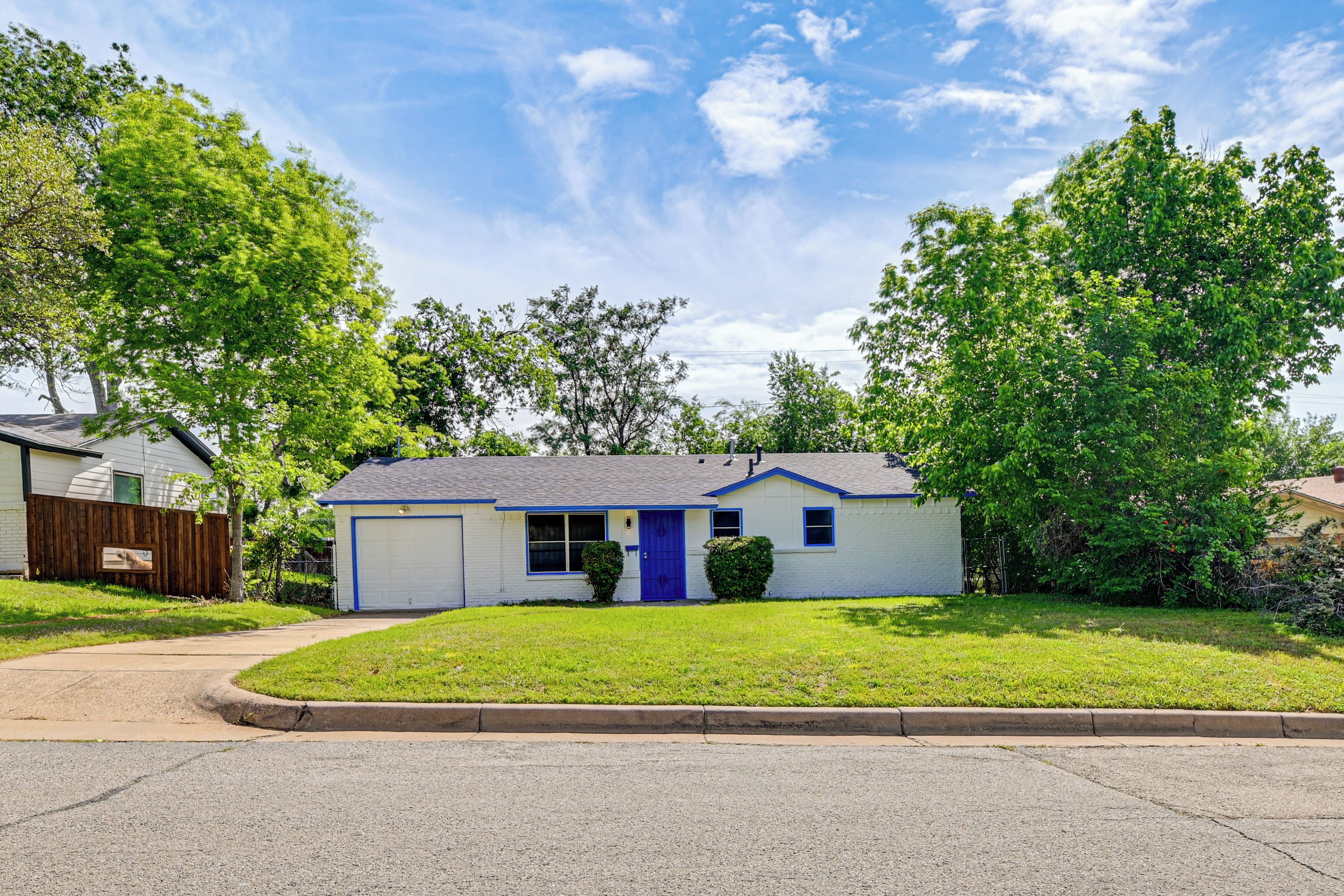 A single-story house with a blue door, a garage, and a well-maintained lawn.