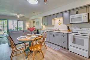 Una cocina moderna con armarios grises, una estufa blanca y un comedor con sillas de madera y una mesa preparada para cuatro.