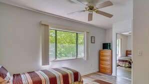 Ein Schlafzimmer mit einem Bett, einem Schminktisch, einem Deckenventilator und einem Fenster mit Blick auf Bäume.