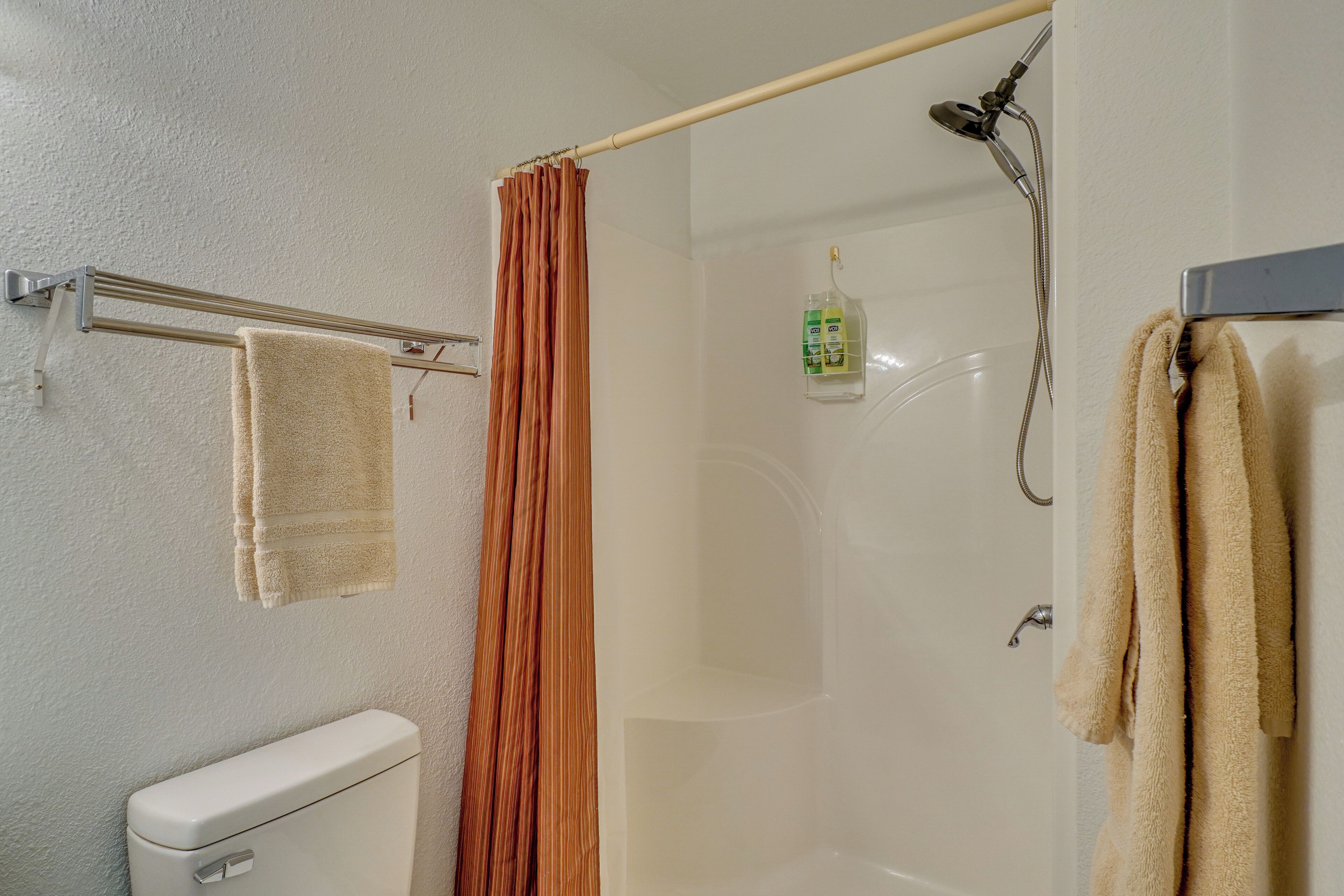 A bathroom with a toilet, a shower with a glass door, and a towel rack with towels.