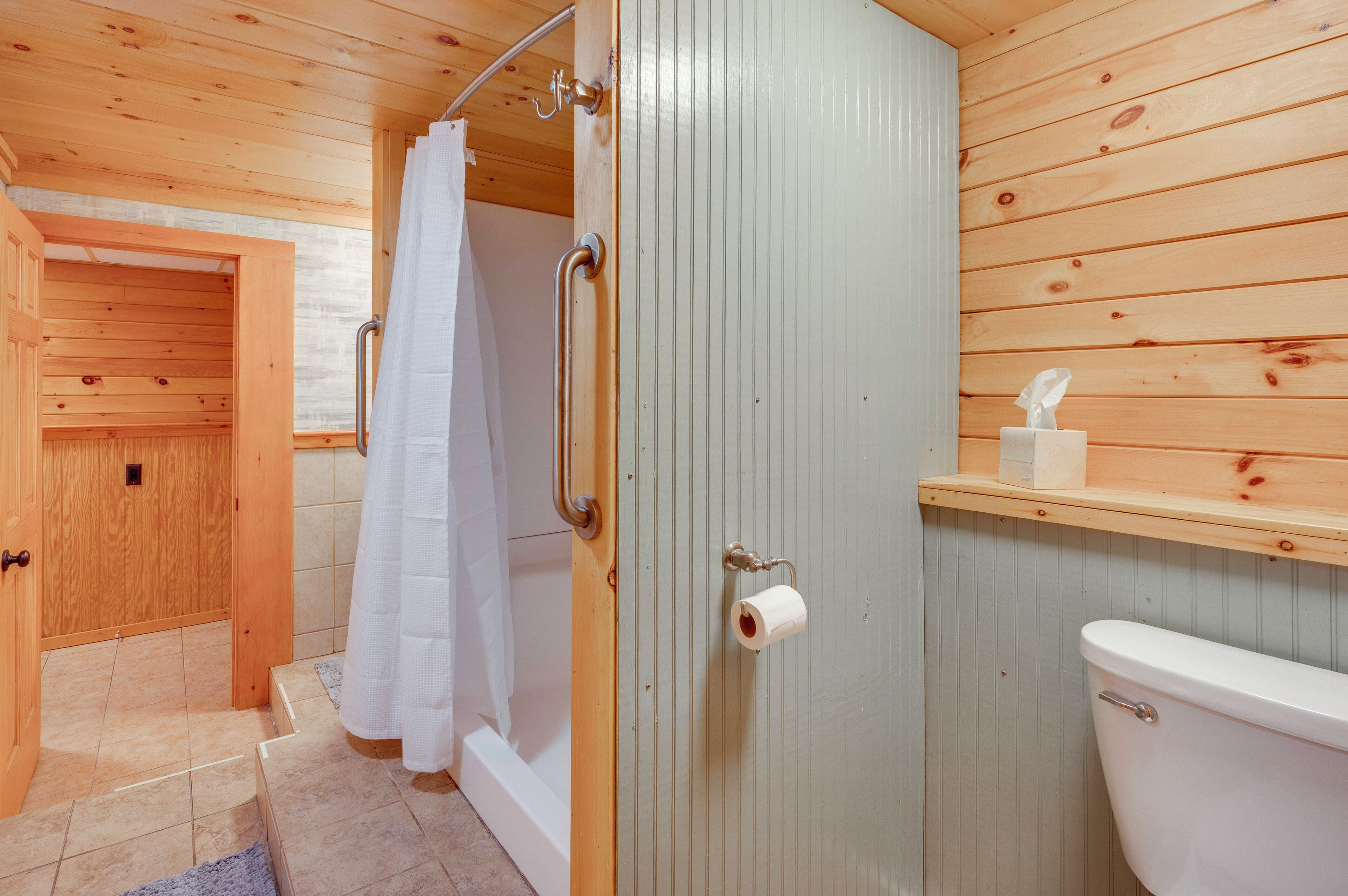 A wooden interior with a shower, toilet, and a door leading to another room.