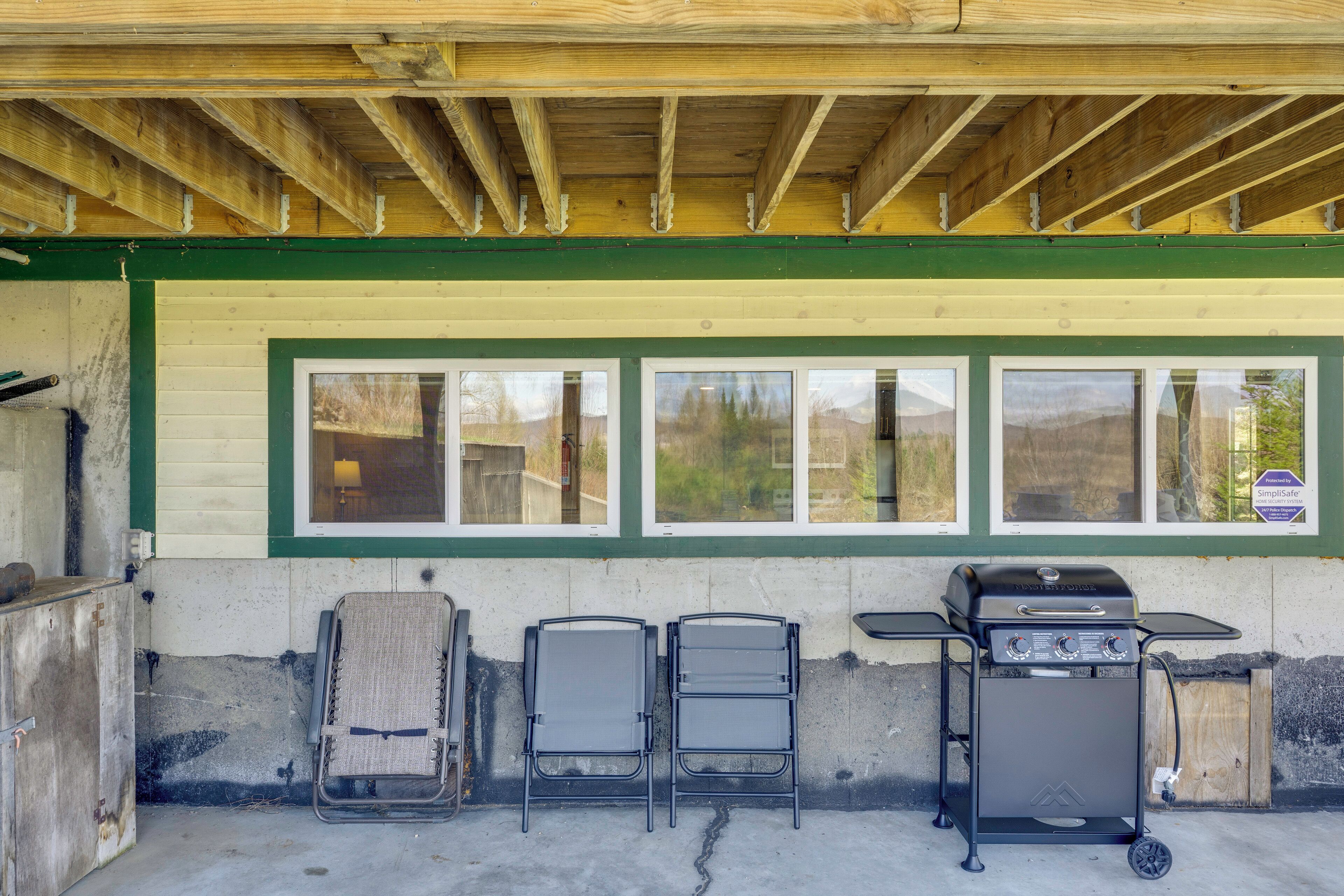 Un espace extérieur abrité, équipé d’un barbecue, de deux chaises et d’un mur vitré.