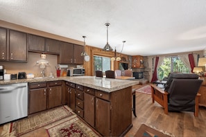 A kitchen with wooden cabinets, a granite countertop, and a dining area with a chair and table.
