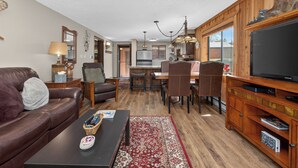 A living room with a leather sofa, a coffee table, a TV, and a dining area with a wooden table and chairs. - Beaver Village Unit #0611 Renovated ground floor family unit clubhouse amenities (Winter Park)