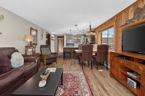A living room with a leather sofa, a coffee table, a TV, and a dining area with a wooden table and chairs.
