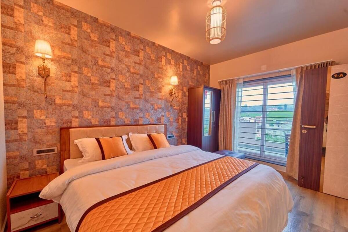 Ein Schlafzimmer mit einem großen Bett, einer Wand mit Steinmuster, zwei Wandleuchten, einem Kleiderschrank und einer Glastür zu einem Balkon.